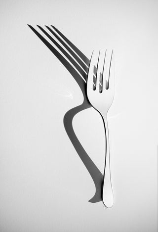Metallic fork casting a shadow on a light gray background